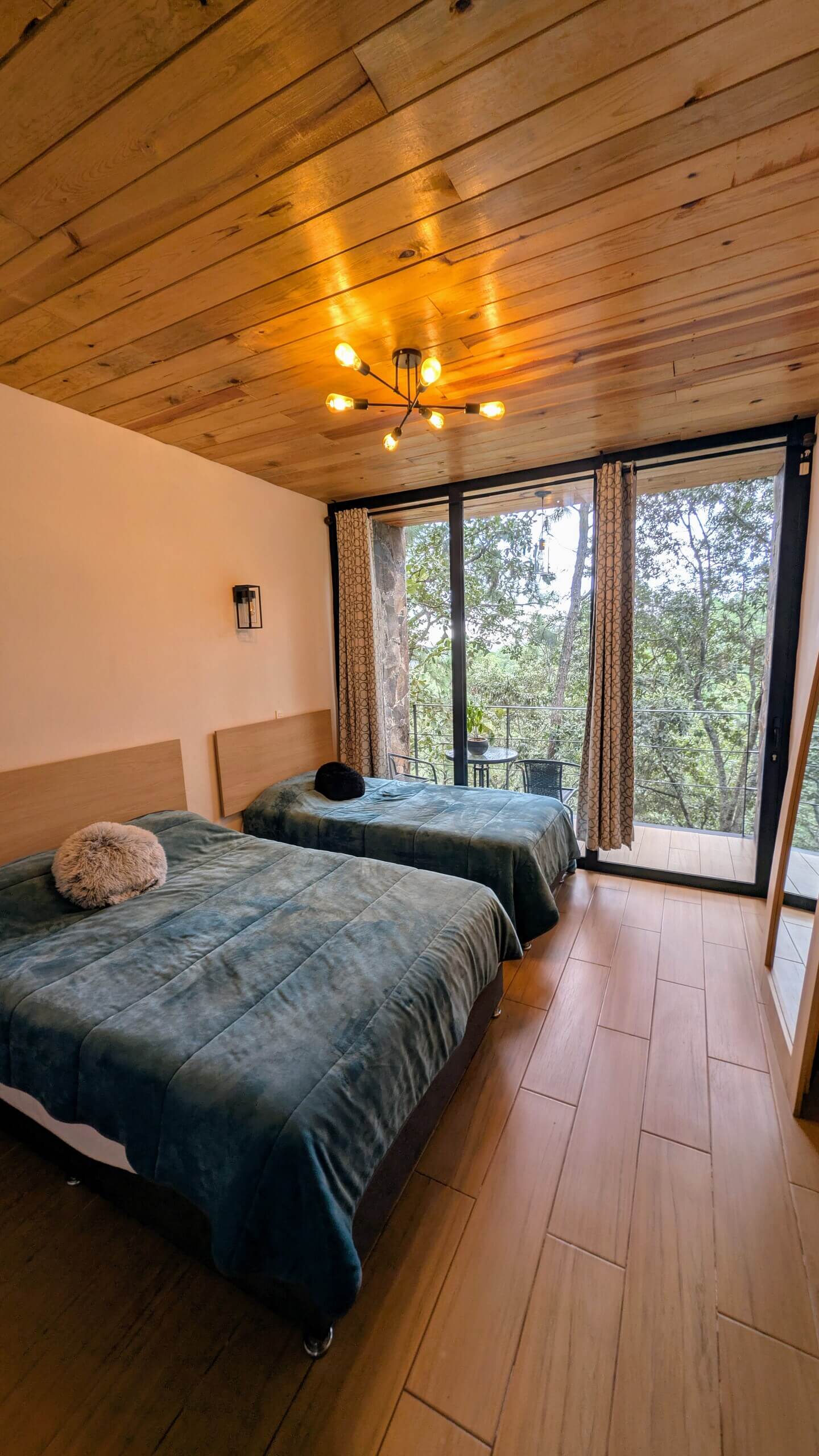 Segunda recámara con cama matrimonial e individual y balcón al bosque